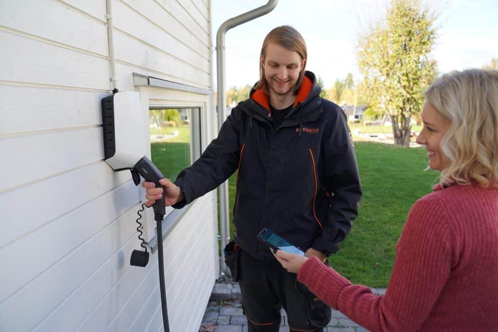 En elektriker som viser kunden hvordan man bruker elbilladeren som har blitt installert hjemme hos kunden.