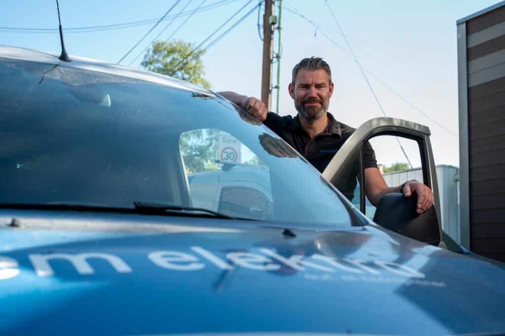 Elektriker fra Elektrikern Majorstua står ved bilen sin med søren åpen og smiler til kameraet.